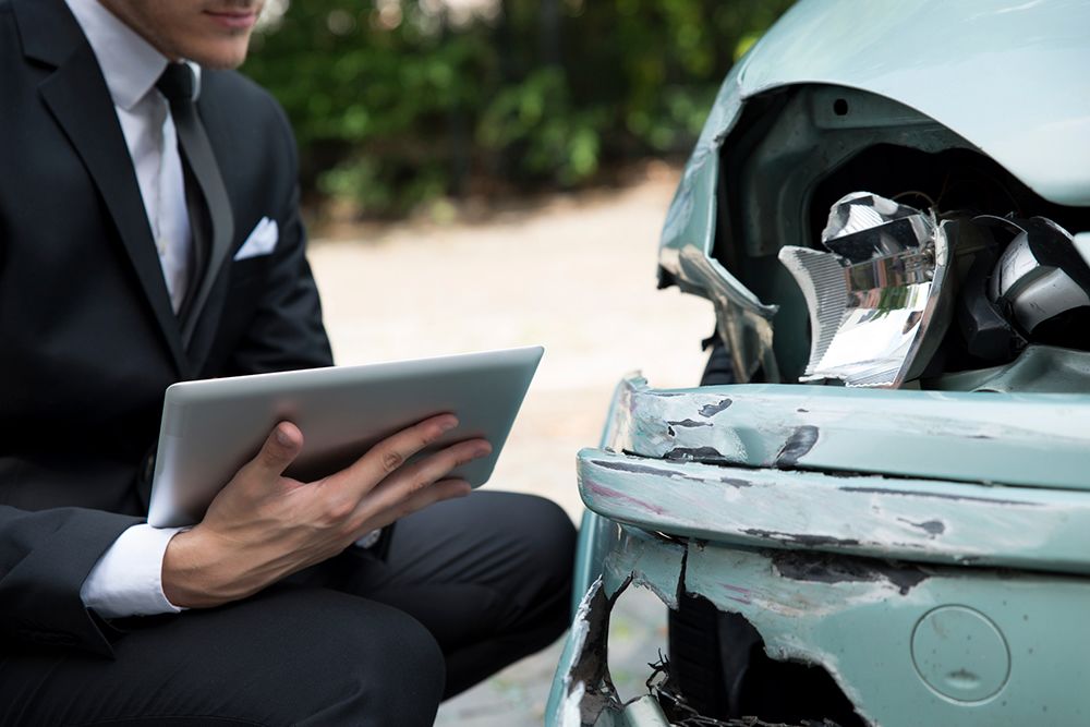 photo of a man in a suit next to a damaged car